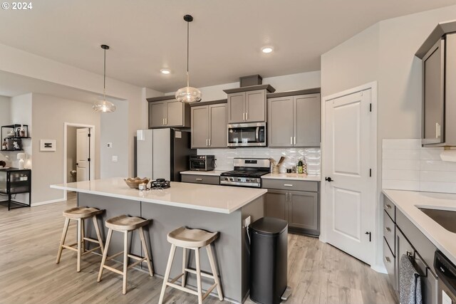 kitchen with stainless steel appliances, a kitchen breakfast bar, tasteful backsplash, gray cabinets, and a kitchen island