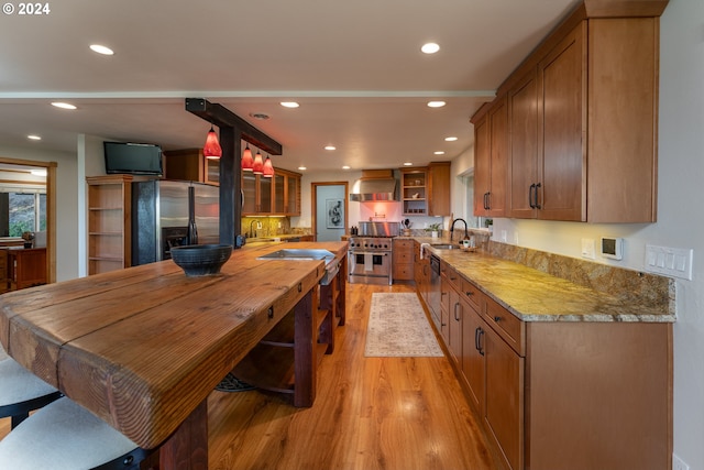 kitchen with wall chimney range hood, light hardwood / wood-style floors, sink, and appliances with stainless steel finishes