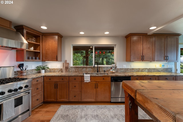 kitchen featuring sink, light stone counters, light wood-type flooring, appliances with stainless steel finishes, and wall chimney range hood