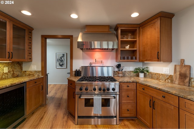 kitchen with beverage cooler, high end stainless steel range, light stone counters, wall chimney exhaust hood, and light hardwood / wood-style flooring