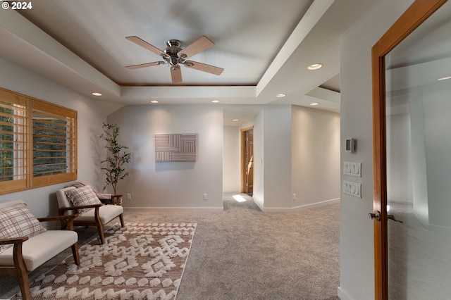 sitting room featuring ceiling fan, a raised ceiling, and light carpet