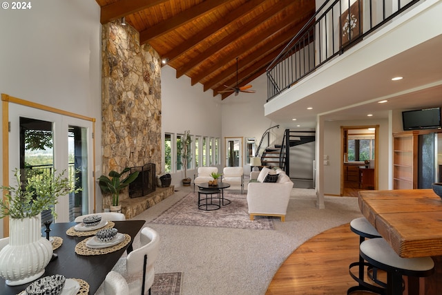 living room featuring a stone fireplace, high vaulted ceiling, beamed ceiling, ceiling fan, and wood ceiling