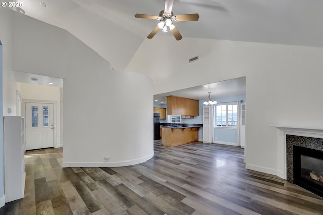 unfurnished living room featuring a tiled fireplace, ceiling fan with notable chandelier, dark hardwood / wood-style floors, and high vaulted ceiling