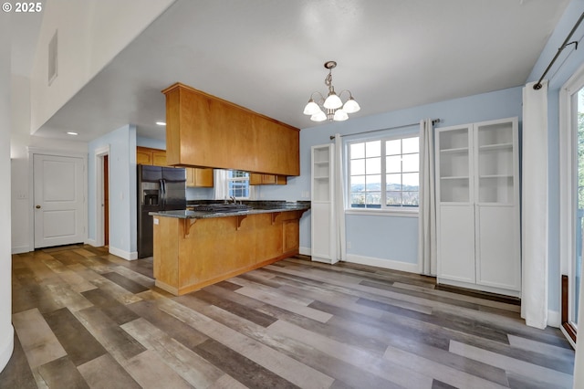 kitchen featuring kitchen peninsula, black fridge with ice dispenser, decorative light fixtures, an inviting chandelier, and a breakfast bar area