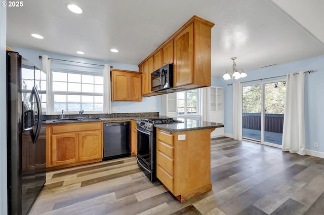 kitchen with black appliances, dark stone counters, light hardwood / wood-style floors, sink, and hanging light fixtures