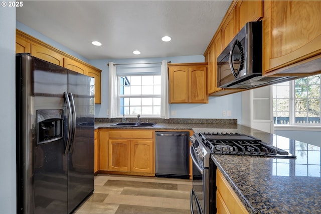 kitchen with plenty of natural light, sink, stainless steel appliances, and dark stone counters