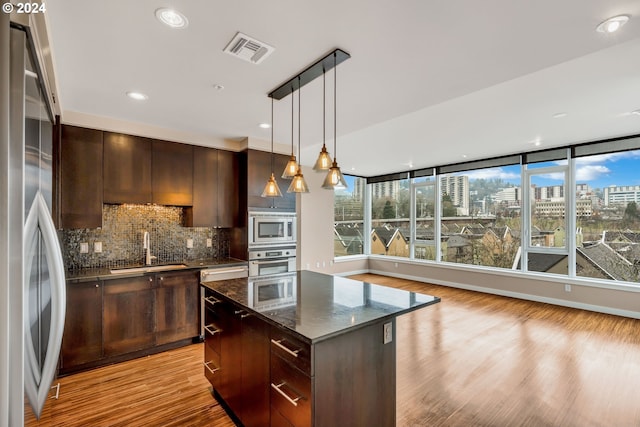 kitchen featuring appliances with stainless steel finishes, light hardwood / wood-style floors, sink, dark stone counters, and a kitchen island