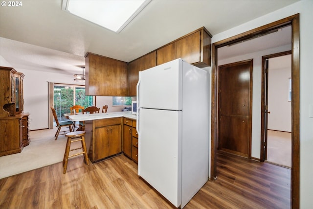 kitchen with kitchen peninsula, a breakfast bar, white fridge, and light wood-type flooring