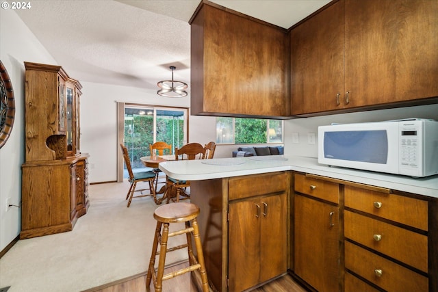 kitchen featuring kitchen peninsula, a kitchen bar, a textured ceiling, light colored carpet, and hanging light fixtures