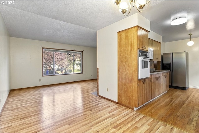 kitchen with light wood-type flooring, a textured ceiling, a notable chandelier, oven, and stainless steel refrigerator with ice dispenser