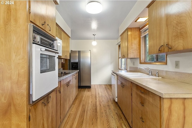 kitchen with white appliances, sink, light hardwood / wood-style floors, and decorative light fixtures