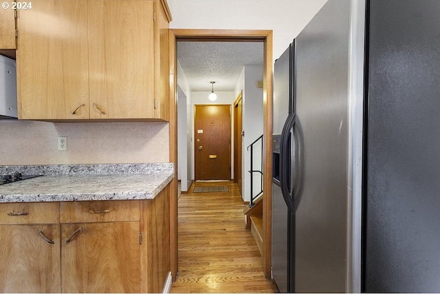 kitchen with a textured ceiling, stainless steel fridge with ice dispenser, hanging light fixtures, light hardwood / wood-style floors, and light stone countertops