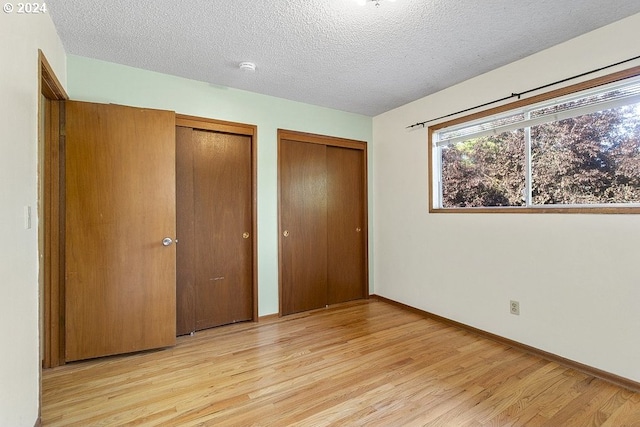 unfurnished bedroom featuring two closets, a textured ceiling, and light hardwood / wood-style floors