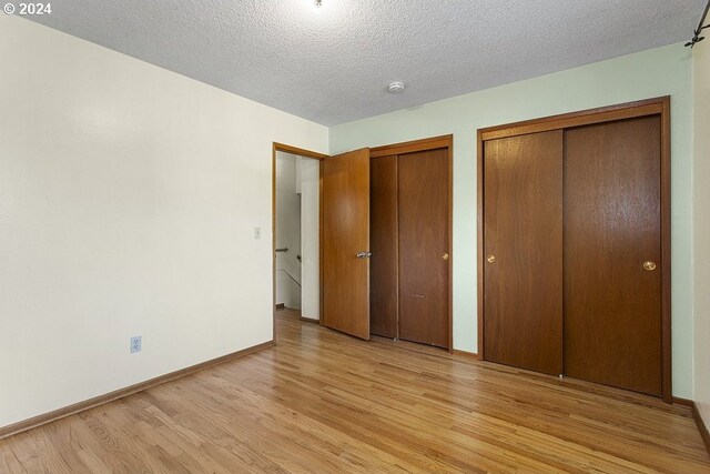 unfurnished bedroom featuring two closets, light hardwood / wood-style flooring, and a textured ceiling