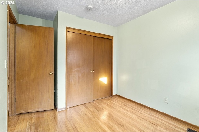 unfurnished bedroom featuring light hardwood / wood-style flooring, a textured ceiling, and a closet