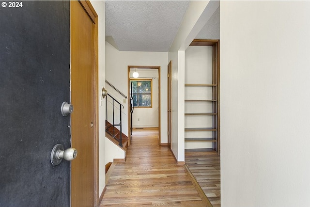 hallway with a textured ceiling and light hardwood / wood-style floors