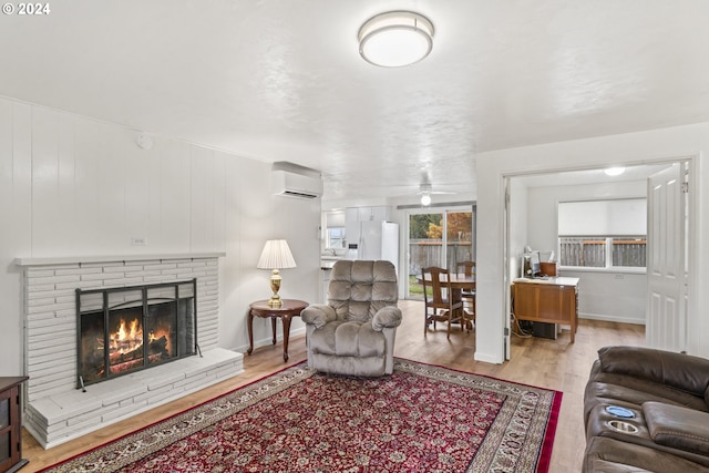 living room with an AC wall unit, light hardwood / wood-style flooring, ceiling fan, and a brick fireplace