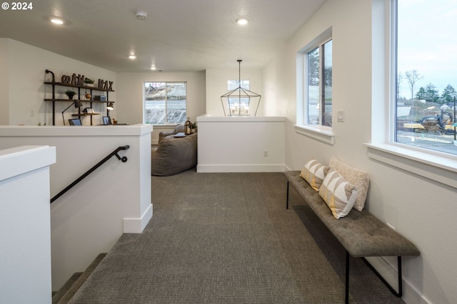 corridor featuring an inviting chandelier and dark colored carpet