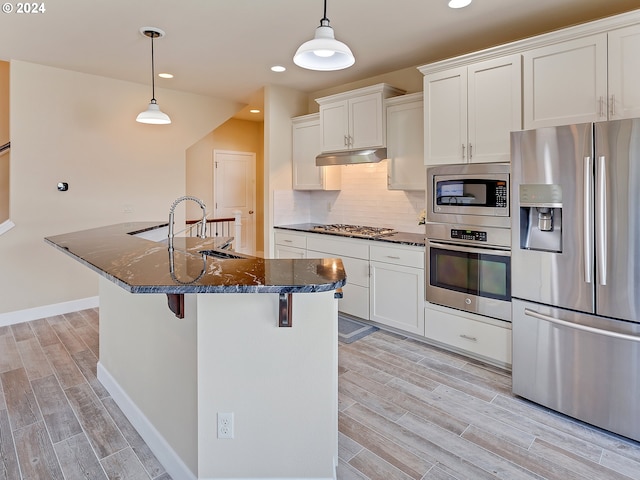 kitchen with a center island with sink, dark stone counters, hanging light fixtures, and stainless steel appliances