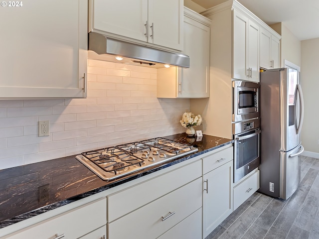 kitchen with appliances with stainless steel finishes, dark hardwood / wood-style floors, dark stone counters, and white cabinetry