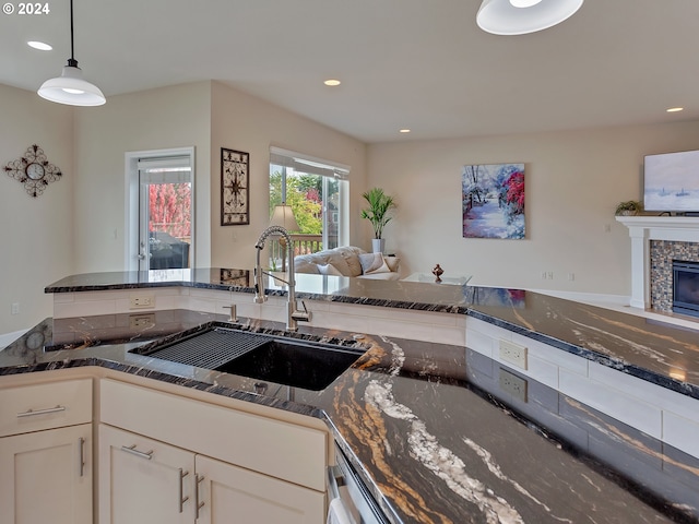 kitchen featuring white cabinets, pendant lighting, sink, dark stone counters, and a fireplace