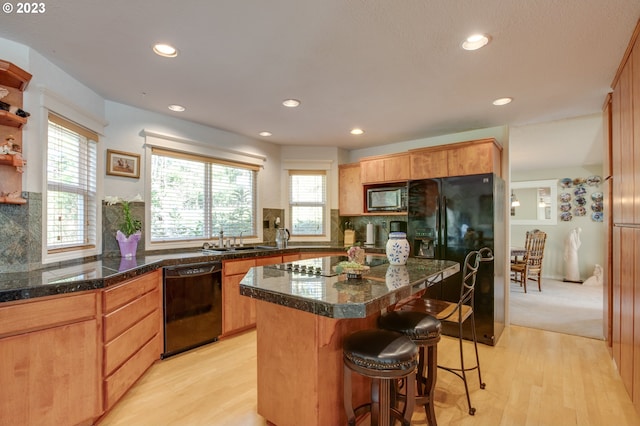 kitchen featuring a kitchen island, a breakfast bar area, black appliances, sink, and light wood-type flooring