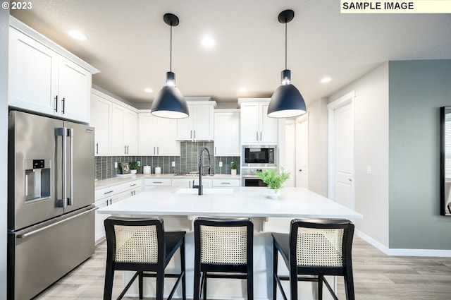 kitchen featuring light wood-type flooring, white cabinetry, stainless steel appliances, and an island with sink