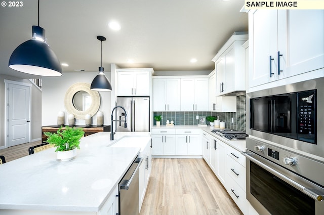 kitchen with white cabinetry, hanging light fixtures, a kitchen island with sink, appliances with stainless steel finishes, and light wood-type flooring