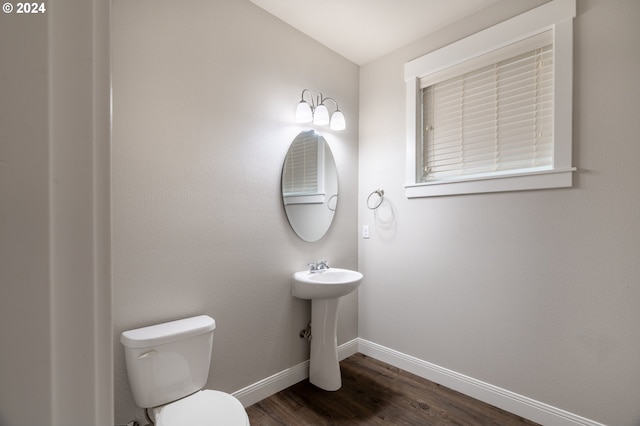 half bath with toilet, baseboards, and wood finished floors