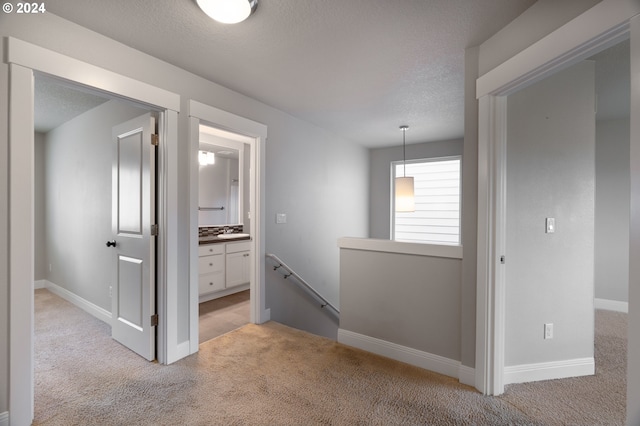 hall with light carpet, baseboards, a textured ceiling, and an upstairs landing