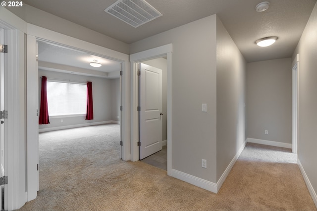 corridor with light carpet and a textured ceiling