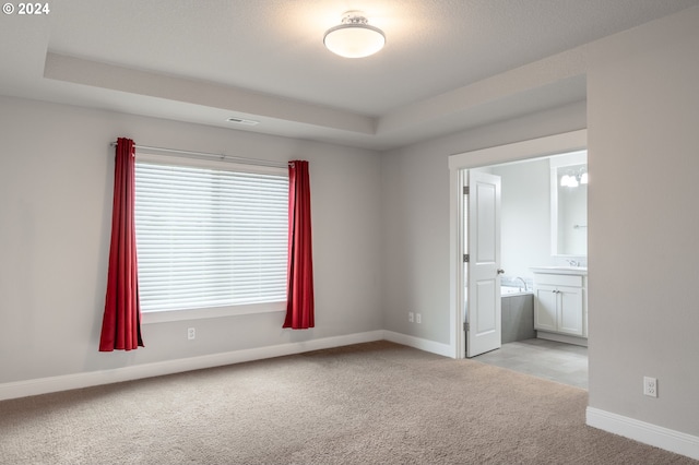 spare room featuring light carpet, a raised ceiling, visible vents, and baseboards