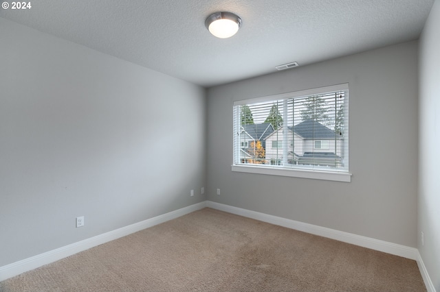 empty room featuring light carpet, baseboards, visible vents, and a textured ceiling