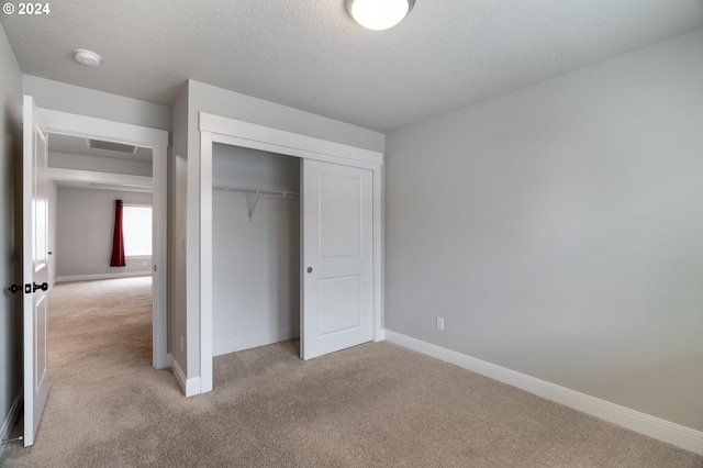 unfurnished bedroom featuring a textured ceiling, light carpet, and a closet