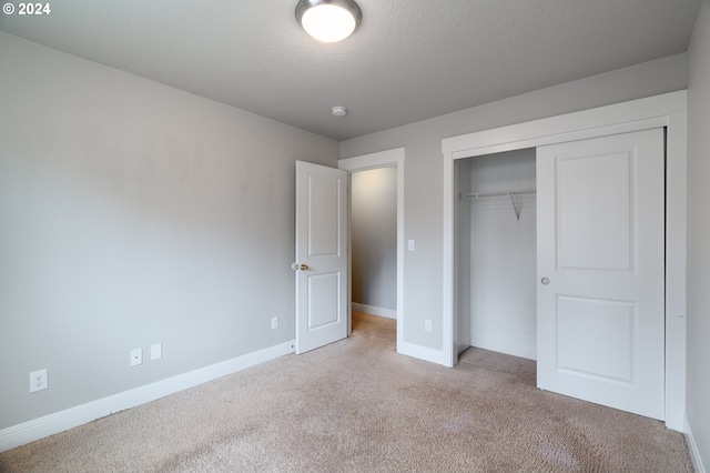 unfurnished bedroom featuring a closet, light colored carpet, a textured ceiling, and baseboards