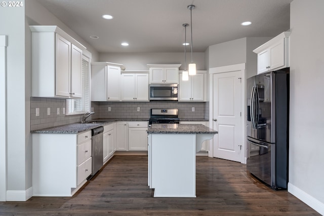 kitchen with a sink, a kitchen island, white cabinets, appliances with stainless steel finishes, and dark stone counters