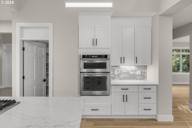 kitchen featuring light stone countertops, light hardwood / wood-style flooring, tasteful backsplash, white cabinetry, and double oven