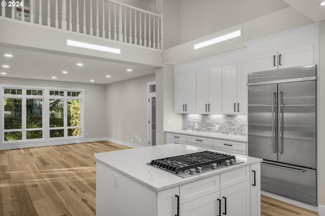 kitchen with appliances with stainless steel finishes, light stone counters, a kitchen island, white cabinetry, and backsplash