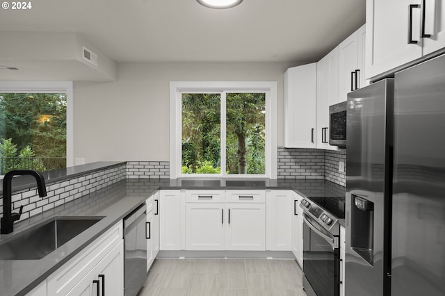 kitchen featuring sink, white cabinets, dark stone countertops, backsplash, and appliances with stainless steel finishes