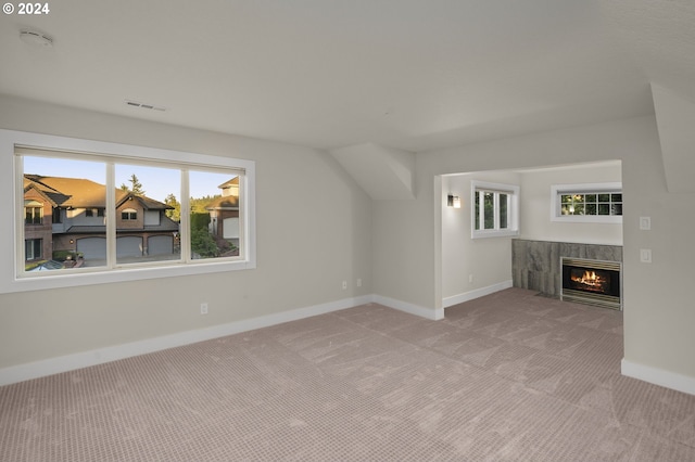 unfurnished living room with a healthy amount of sunlight, a premium fireplace, vaulted ceiling, and light carpet