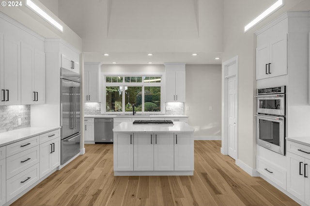 kitchen with a kitchen island, white cabinets, light wood-type flooring, and appliances with stainless steel finishes