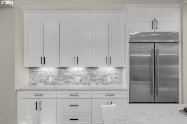 kitchen with white cabinets, built in fridge, backsplash, and light stone countertops