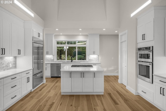 kitchen featuring a center island, stainless steel appliances, tasteful backsplash, light wood-type flooring, and white cabinets