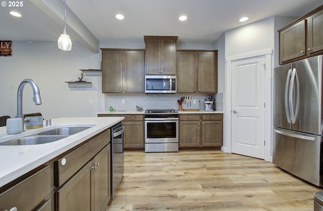 kitchen featuring hanging light fixtures, sink, light hardwood / wood-style flooring, appliances with stainless steel finishes, and tasteful backsplash