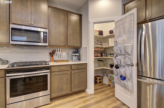 kitchen featuring light countertops, light wood-style flooring, decorative backsplash, and appliances with stainless steel finishes