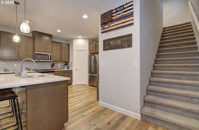 kitchen featuring pendant lighting, a breakfast bar, backsplash, appliances with stainless steel finishes, and light hardwood / wood-style floors