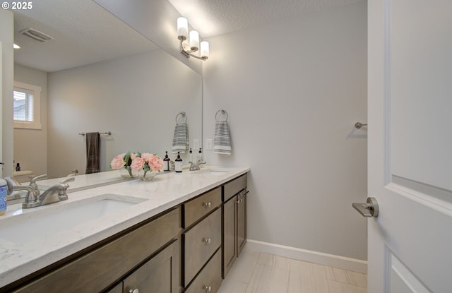 bathroom featuring double vanity, a sink, visible vents, and a textured ceiling