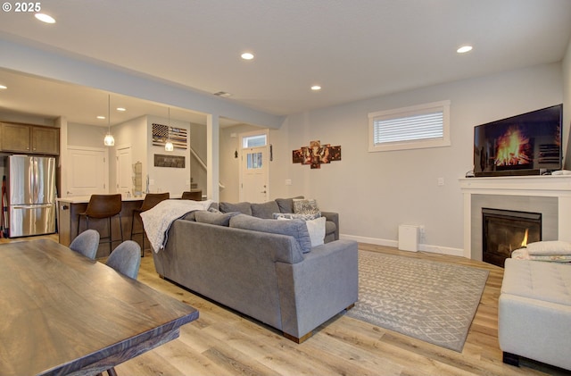 living room featuring stairway, light wood finished floors, a glass covered fireplace, baseboards, and recessed lighting