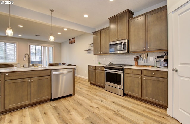 kitchen featuring light countertops, appliances with stainless steel finishes, a sink, light wood-style floors, and backsplash