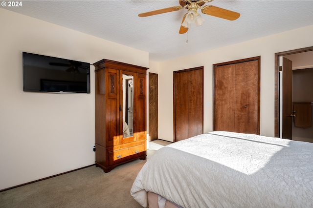 bedroom with a textured ceiling, ceiling fan, light colored carpet, and two closets